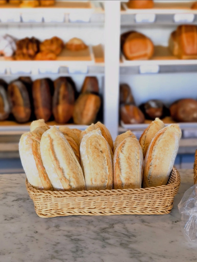 Freshly baked artisan baguettes in counter basket in front of bread shelves